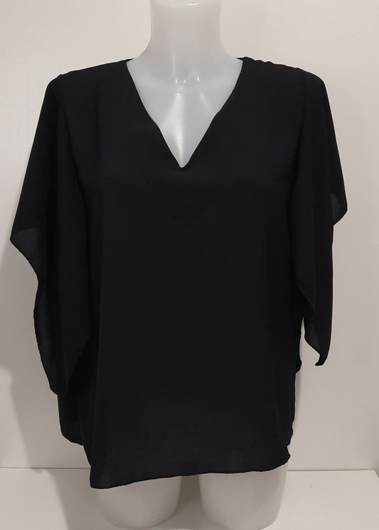 Femme portant un top fluide noir à col V et manches papillon, coupe droite fluide en polyester léger, taille unique 36–42 – style élégant et moderne.