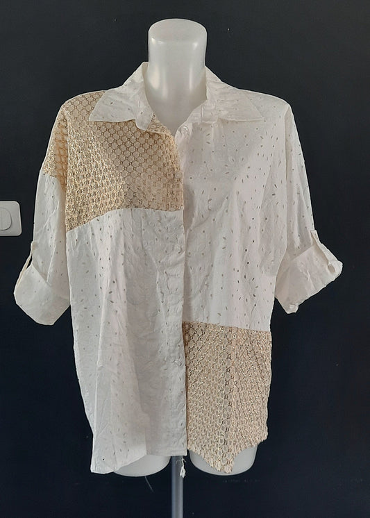 Chemise blanche en broderie anglaise avec empiècements en crochet doré sur l’épaule, le devant et le bas. Manches retroussables, coupe asymétrique pour un look bohème moderne.