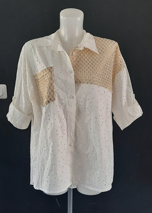 Chemise blanche en broderie anglaise avec empiècements en crochet doré sur l’épaule et la poitrine. Coupe ample, manches retroussables, style bohème chic parfait pour l'été.