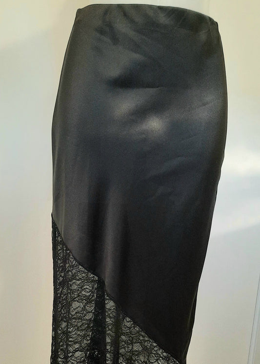 Jupe longue noire en satin avec empiècement asymétrique en dentelle transparente à la base. Coupe droite et élégante, idéale pour une tenue de soirée ou une occasion spéciale.