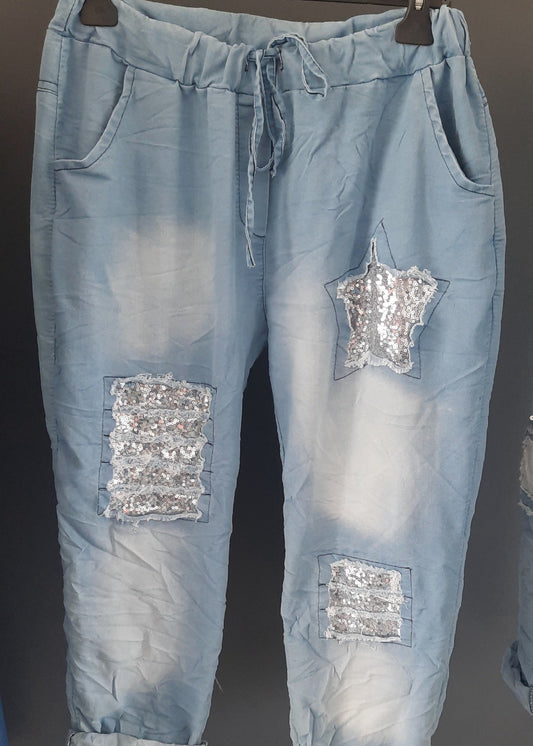 Pantalon jogger bleu clair pour femme, coupe décontractée avec taille élastique et lien à nouer, décoré de patchs à sequins argentés dont une étoile brillante. Style casual tendance avec une touche d’originalité.