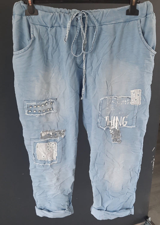Pantalon jogging bleu clair pour femme, coupe décontractée avec taille élastique et lien de serrage, décoré de patchs brodés, clous et sequins argentés. Style streetwear tendance et confortable.