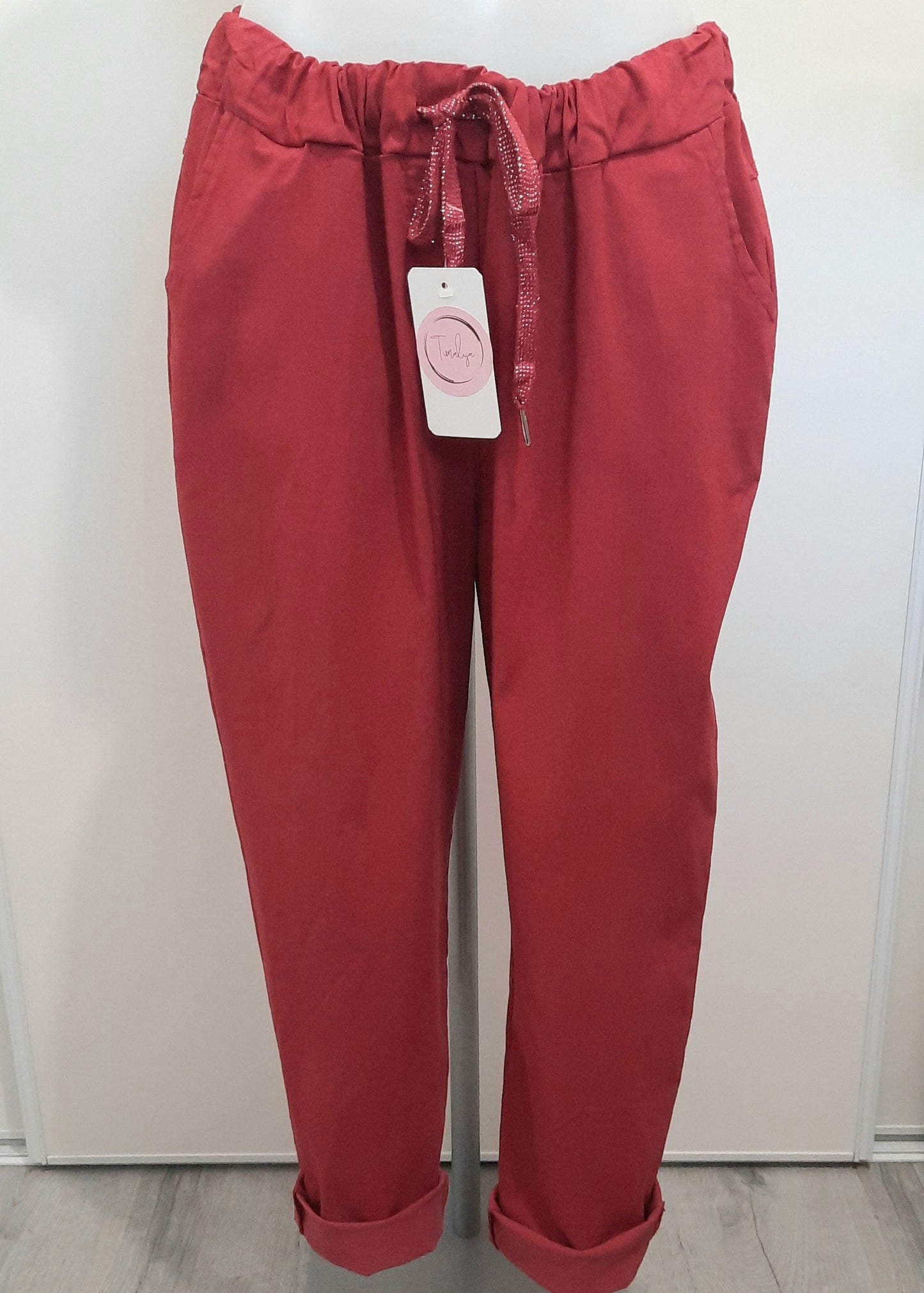 Pantalon magique femme coupe carotte en tissu fluide bordeaux, taille élastiquée avec cordon brillant à nouer, poches latérales et bas retroussés. Style décontracté et tendance.