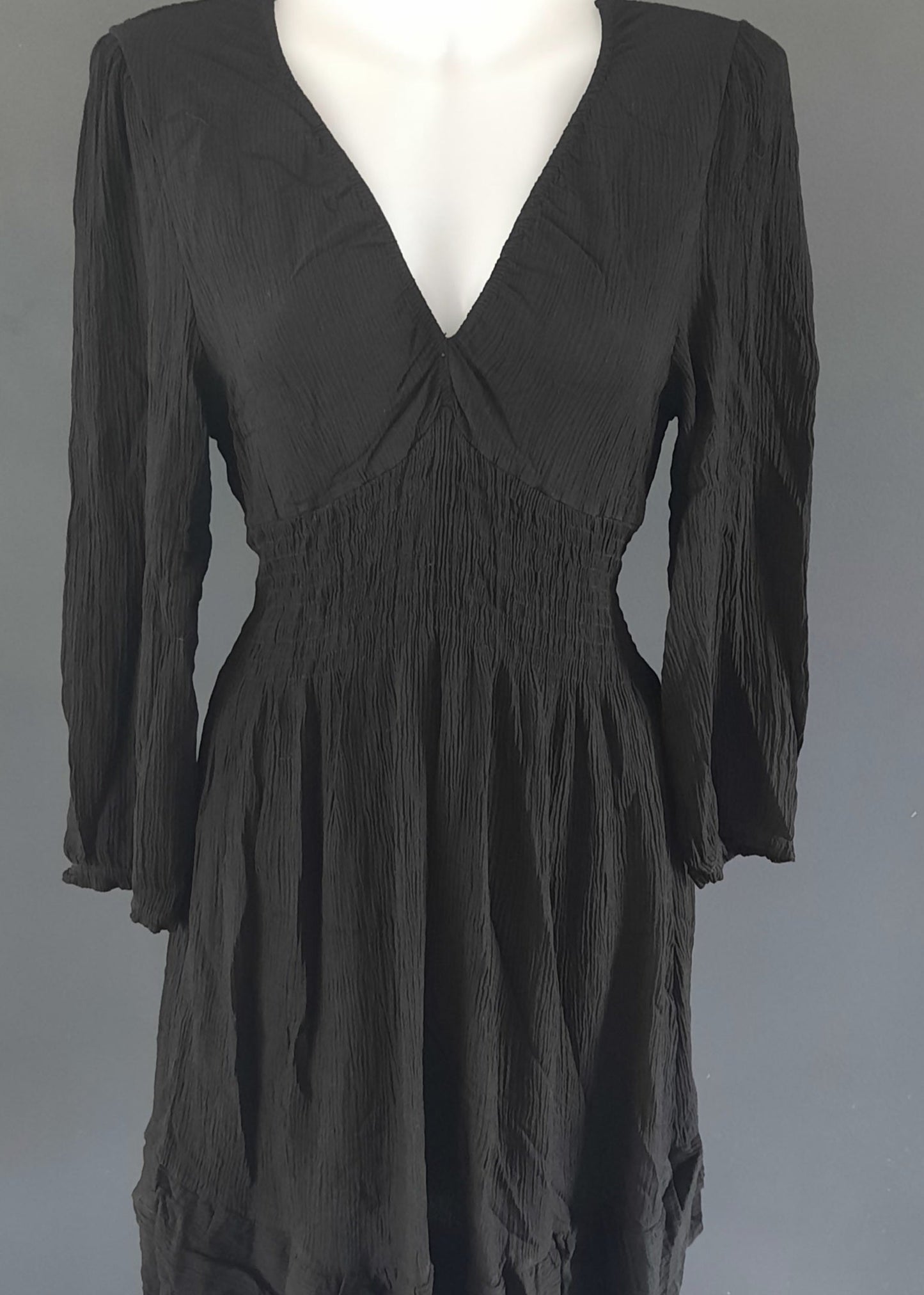 Robe courte noire à manches longues, en tissu gaufré, avec un décolleté cache-cœur et une taille smockée. Coupe fluide et féminine, idéale pour le printemps ou l’été.