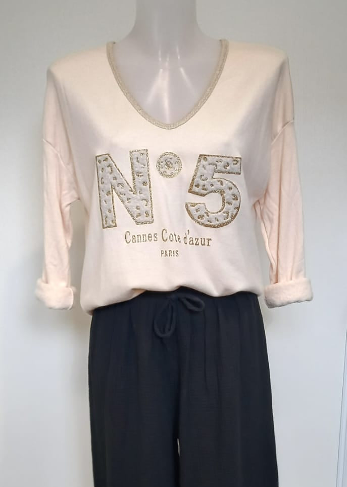 T-shirt beige à manches longues pour femme, col en V avec bord lurex doré, inscription 'N°5 Cannes Côte d’Azur Paris' en relief léopard et doré. Style casual chic inspiré des tendances parisiennes.