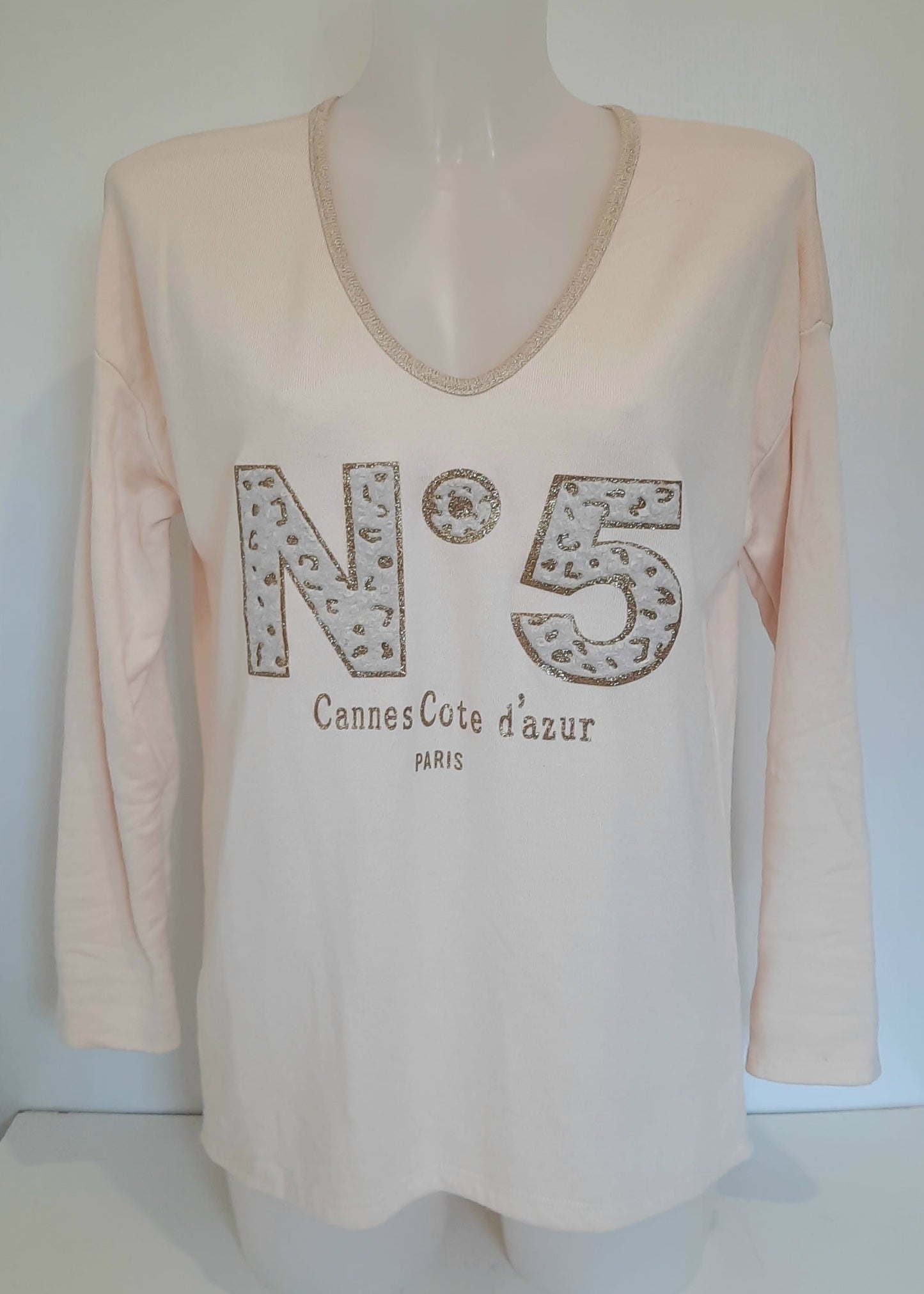 T-shirt beige à manches longues pour femme, col en V avec bord lurex doré, inscription 'N°5 Cannes Côte d’Azur Paris' en relief léopard et doré. Style casual chic inspiré des tendances parisiennes.
