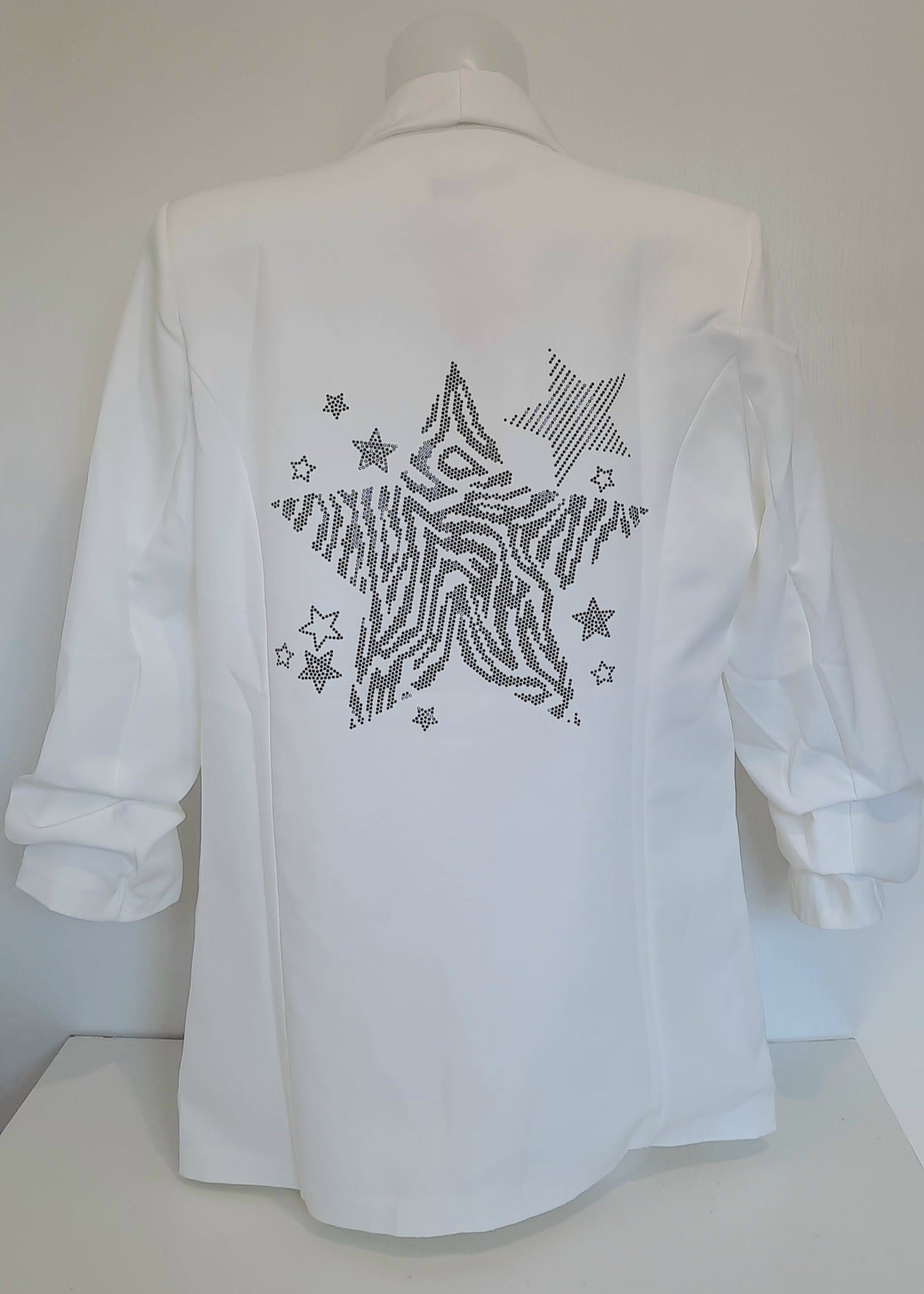 Veste tailleur femme blanche avec manches 3/4 froncées, coupe droite et fluide, poches à rabat décoratives, et grand motif étoile en strass noirs au dos. Un blazer chic et original de la collection Timalya prêt-à-porter féminin.