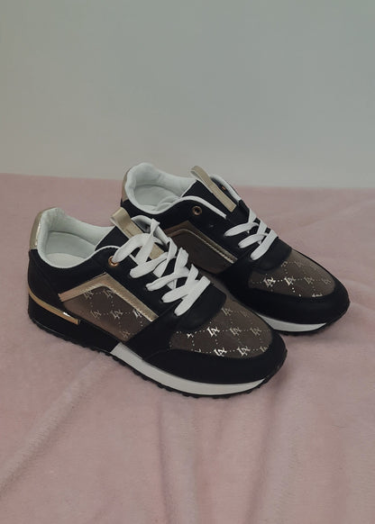 Baskets femme noires et marron avec détails dorés, imprimé monogramme doré, semelle blanche et noire, lacets blancs et œillets dorés. Un modèle chic et urbain – collection Timalya chaussures.