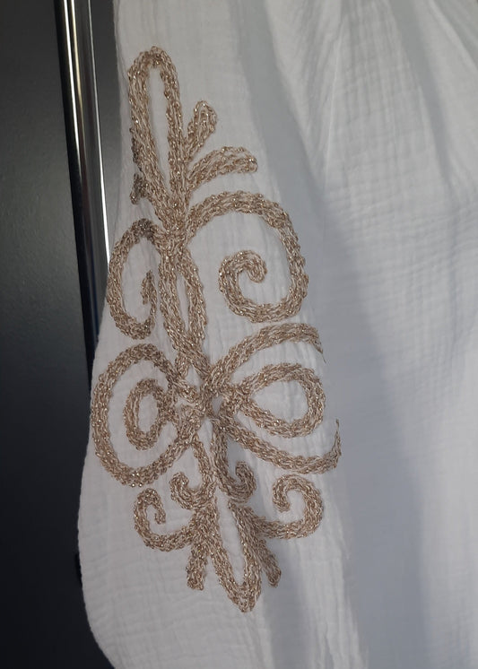 Blouse blanche en gaze de coton pour femme, manches 3/4 avec broderies dorées sur les bras, encolure tunisienne et boutonnage frontal. Style bohème chic et léger.