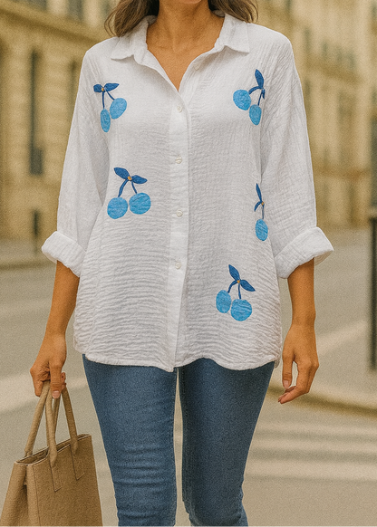 Chemise blanche en gaze de coton pour femme, ornée de broderies cerises bleues avec strass – modèle à manches longues retroussables et col classique pour un style estival et ludique.