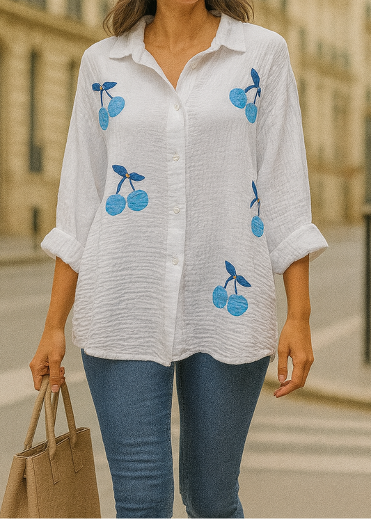 Chemise blanche en gaze de coton pour femme, ornée de broderies cerises bleues avec strass – modèle à manches longues retroussables et col classique pour un style estival et ludique.