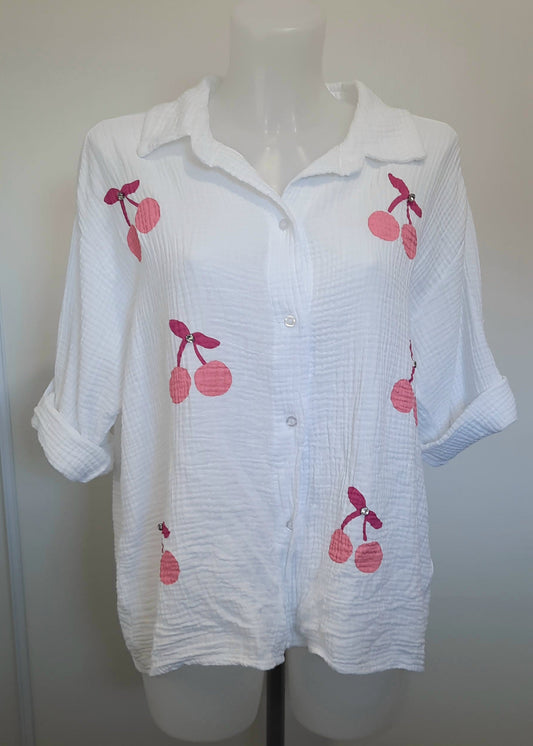 Chemise blanche en gaze de coton pour femme, ornée de broderies cerises roses avec strass – modèle à manches longues retroussables et col classique pour un style estival et ludique.