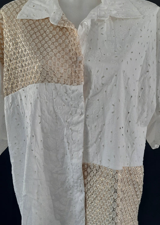 Chemise blanche en broderie anglaise avec empiècements en crochet doré sur l’épaule, le devant et le bas. Manches retroussables, coupe asymétrique pour un look bohème moderne.