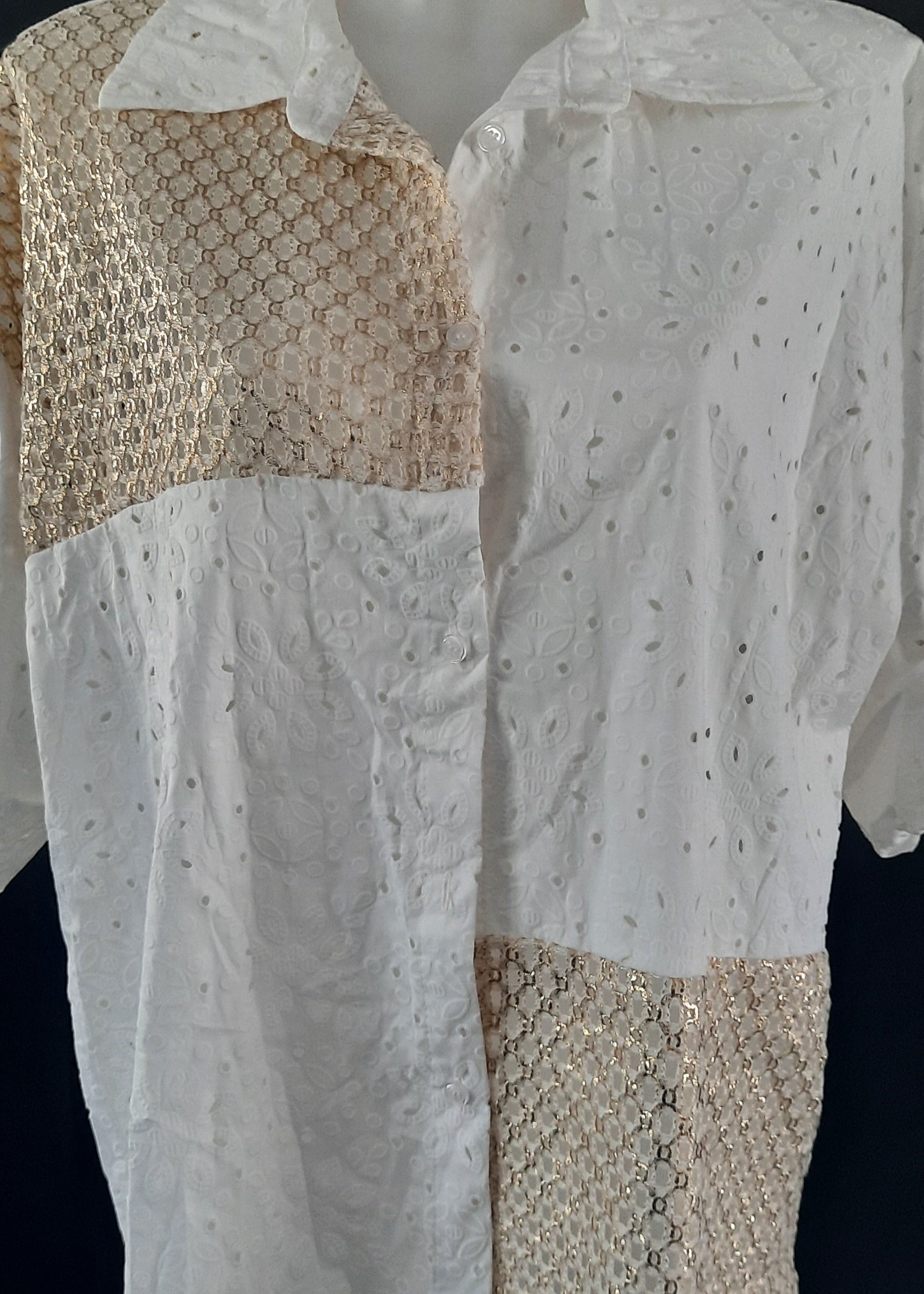 Chemise blanche en broderie anglaise avec empiècements en crochet doré sur l’épaule, le devant et le bas. Manches retroussables, coupe asymétrique pour un look bohème moderne.