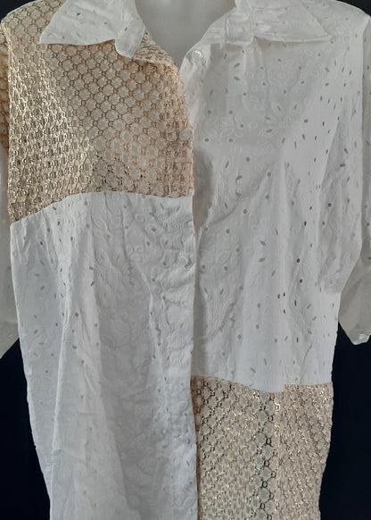 Chemise blanche en broderie anglaise avec empiècements en crochet doré sur l’épaule, le devant et le bas. Manches retroussables, coupe asymétrique pour un look bohème moderne.