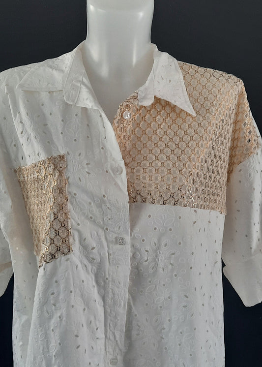 Chemise blanche en broderie anglaise avec empiècements en crochet doré sur l’épaule et la poitrine. Coupe ample, manches retroussables, style bohème chic parfait pour l'été.