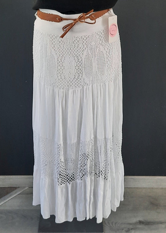Jupe blanche longue à volants, ornée d’empiècements en dentelle ajourée, portée avec une ceinture camel et un haut rose. Style bohème chic, idéale pour la mi-saison.