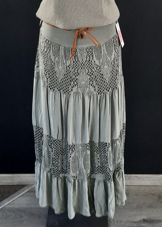 Jupe kaki longue à volants, ornée d’empiècements en dentelle ajourée, portée avec une ceinture camel et un haut rose. Style bohème chic, idéale pour la mi-saison.