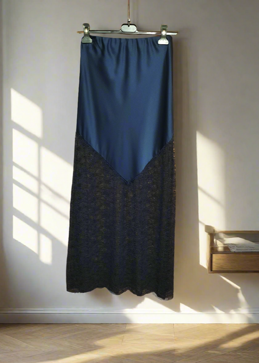 Jupe longue bleu marine en satin avec empiècement asymétrique en dentelle transparente à la base. Coupe droite et élégante, idéale pour une tenue de soirée ou une occasion spéciale.