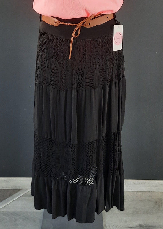 Jupe noire longue à volants, ornée d’empiècements en dentelle ajourée, portée avec une ceinture camel et un haut rose. Style bohème chic, idéale pour la mi-saison.