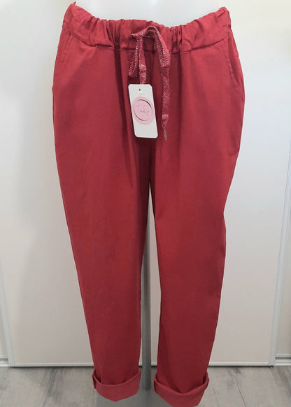 Pantalon magique femme coupe carotte en tissu fluide bordeaux, taille élastiquée avec cordon brillant à nouer, poches latérales et bas retroussés. Style décontracté et tendance.
