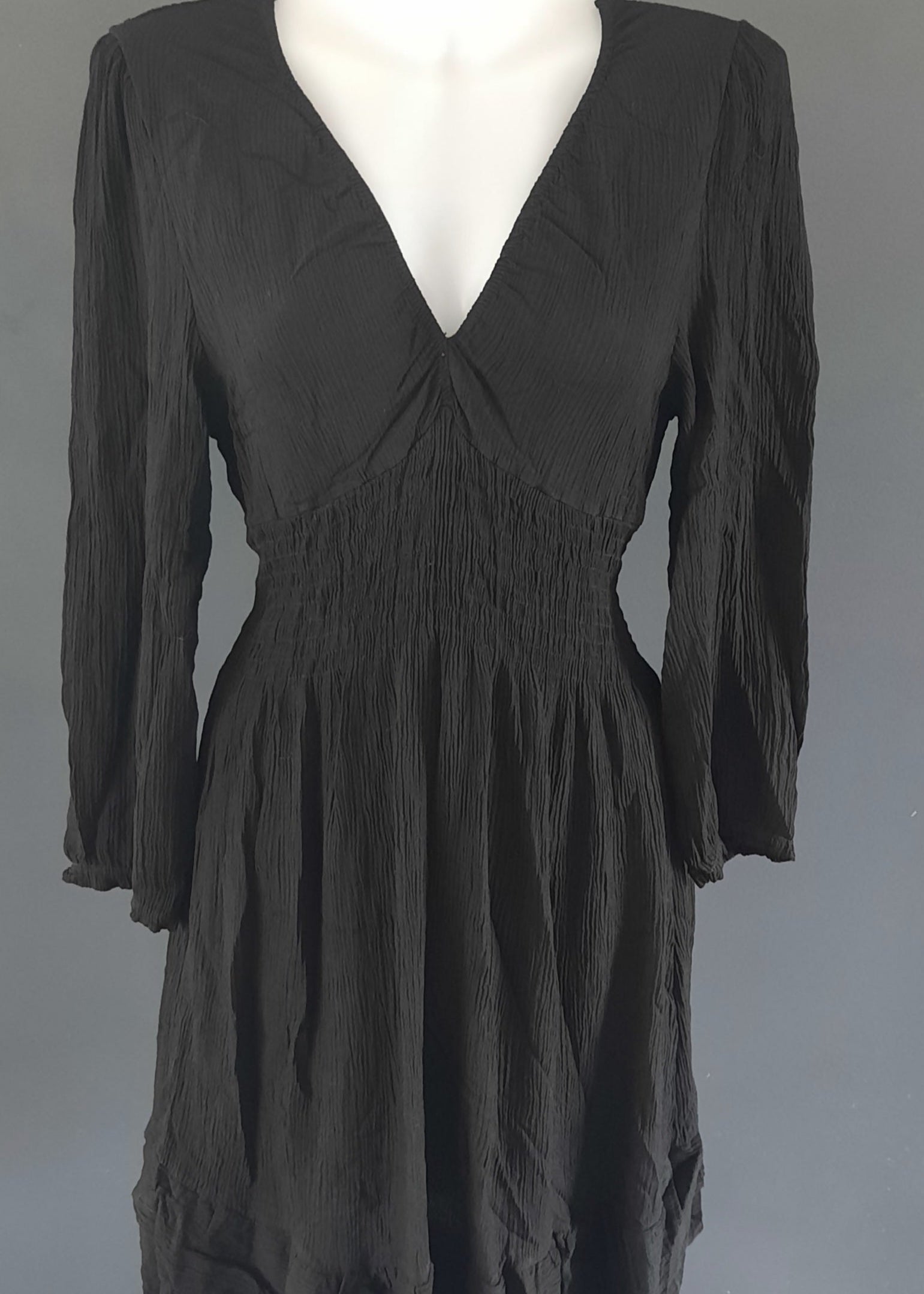 Robe courte noire à manches longues, en tissu gaufré, avec un décolleté cache-cœur et une taille smockée. Coupe fluide et féminine, idéale pour le printemps ou l’été.