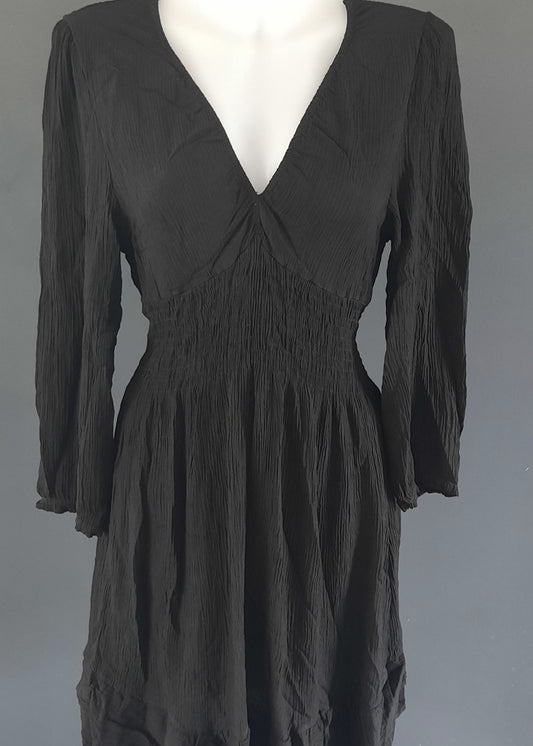 Robe courte noire à manches longues, en tissu gaufré, avec un décolleté cache-cœur et une taille smockée. Coupe fluide et féminine, idéale pour le printemps ou l’été.