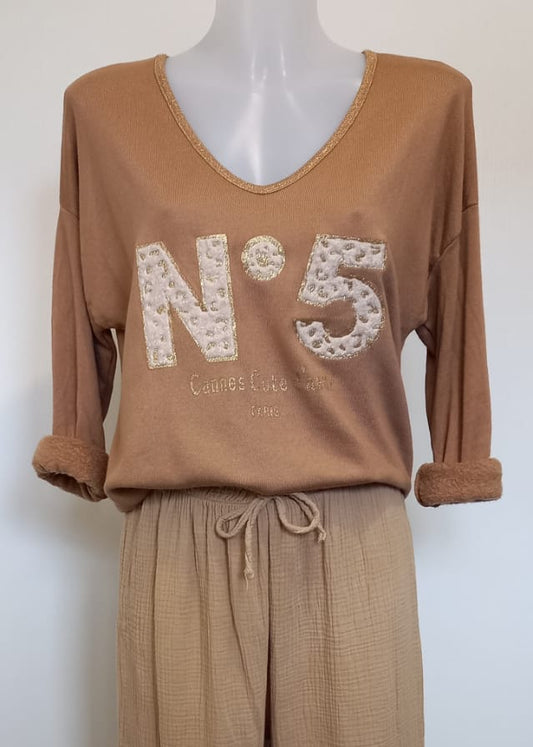 T-shirt camel à manches longues pour femme, col en V avec bord lurex doré, inscription 'N°5 Cannes Côte d’Azur Paris' en relief léopard et doré. Style casual chic inspiré des tendances parisiennes.