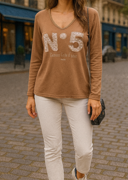 T-shirt camel à manches longues pour femme, col en V avec bord lurex doré, inscription 'N°5 Cannes Côte d’Azur Paris' en relief léopard et doré. Style casual chic inspiré des tendances parisiennes.
