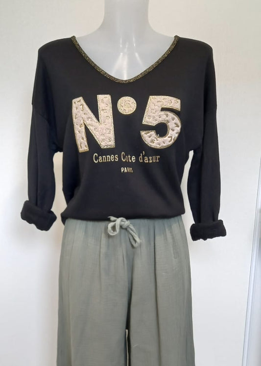 T-shirt noir à manches longues pour femme, col en V avec bord lurex doré, inscription 'N°5 Cannes Côte d’Azur Paris' en relief léopard et doré. Style casual chic inspiré des tendances parisiennes.