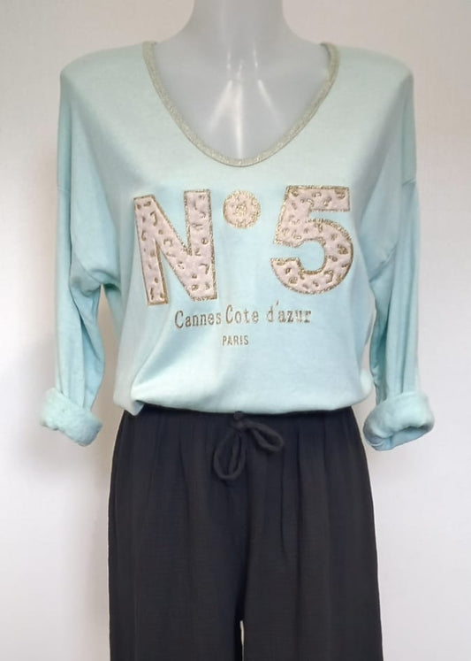 T-shirt vert d'eau à manches longues pour femme, col en V avec bord lurex doré, inscription 'N°5 Cannes Côte d’Azur Paris' en relief léopard et doré. Style casual chic inspiré des tendances parisiennes.