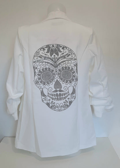 Veste tailleur femme blanche avec coupe droite, manches 3/4 froncées, poches à rabat décoratives et grand motif tête de mort mexicaine en strass noirs dans le dos. Un blazer original et stylé signé Timalya prêt-à-porter féminin.