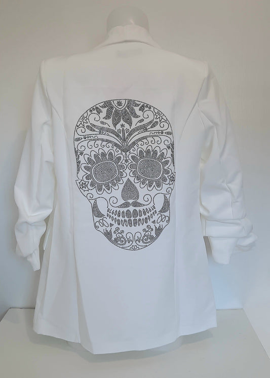 Veste tailleur femme blanche avec coupe droite, manches 3/4 froncées, poches à rabat décoratives et grand motif tête de mort mexicaine en strass noirs dans le dos. Un blazer original et stylé signé Timalya prêt-à-porter féminin.